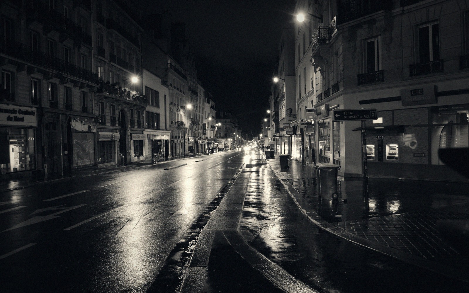 A wet Left Bank street at night, café lights reflected on the pavement